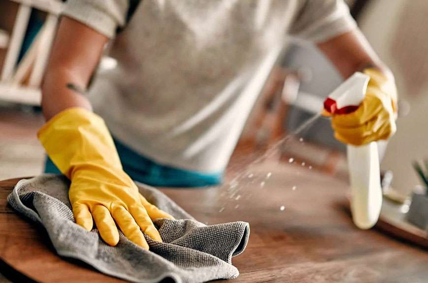 Eldivenli bir el, masayı sprey ve bezle siliyor